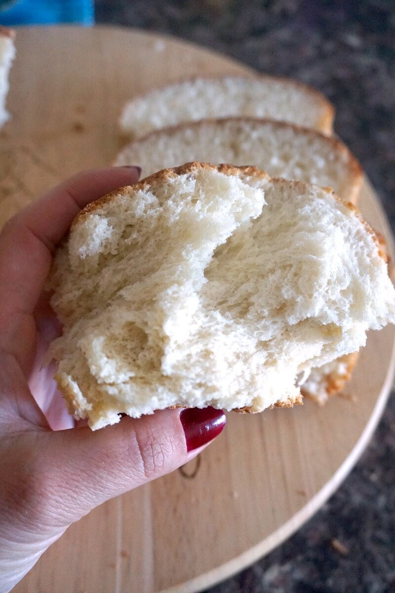 A hand holding a piece of brioche bread to show how fluffy it is inside