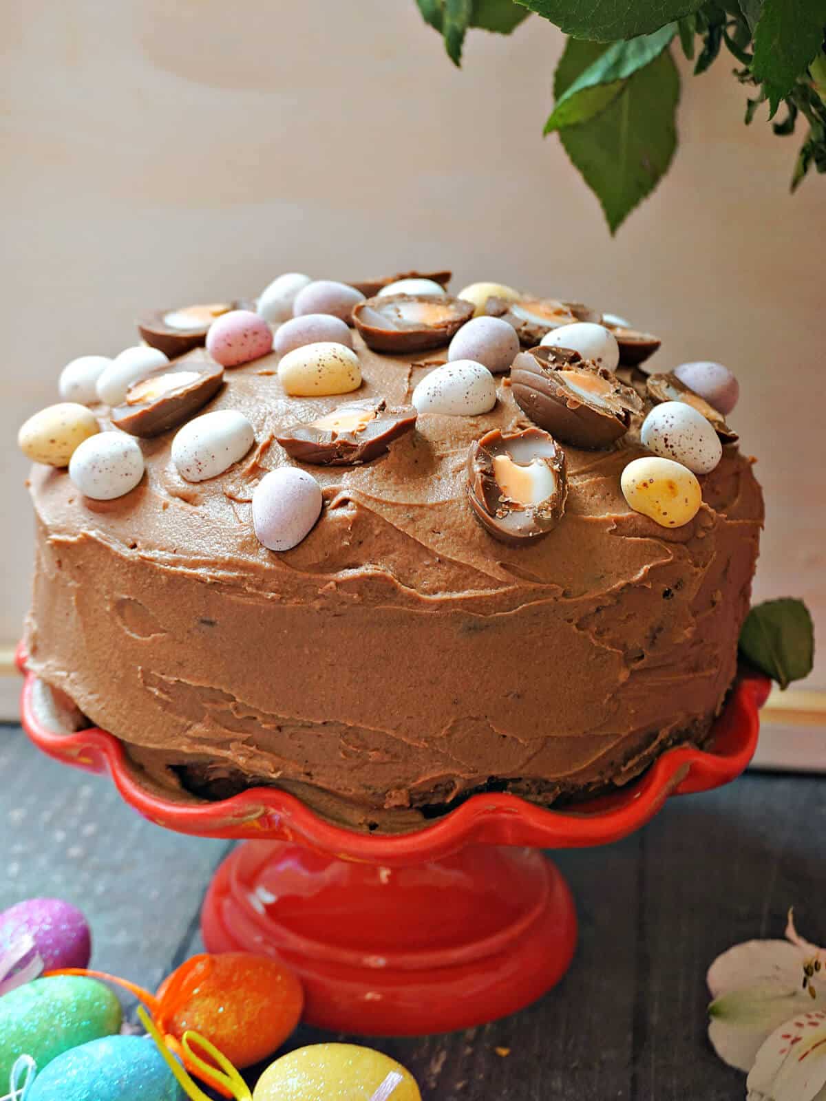 A chocolate cake topped with easter eggs on a red cake stand.