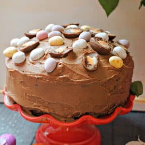 A red cake stand with a chocolate cake decorated with Easter eggs