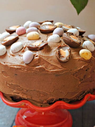 A red cake stand with a chocolate cake decorated with Easter eggs