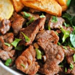 Steak bites, potato wedges and baby spinach leaves on a plate.