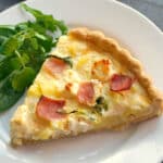 A slice of quiche on a white plate with a green salad on the side