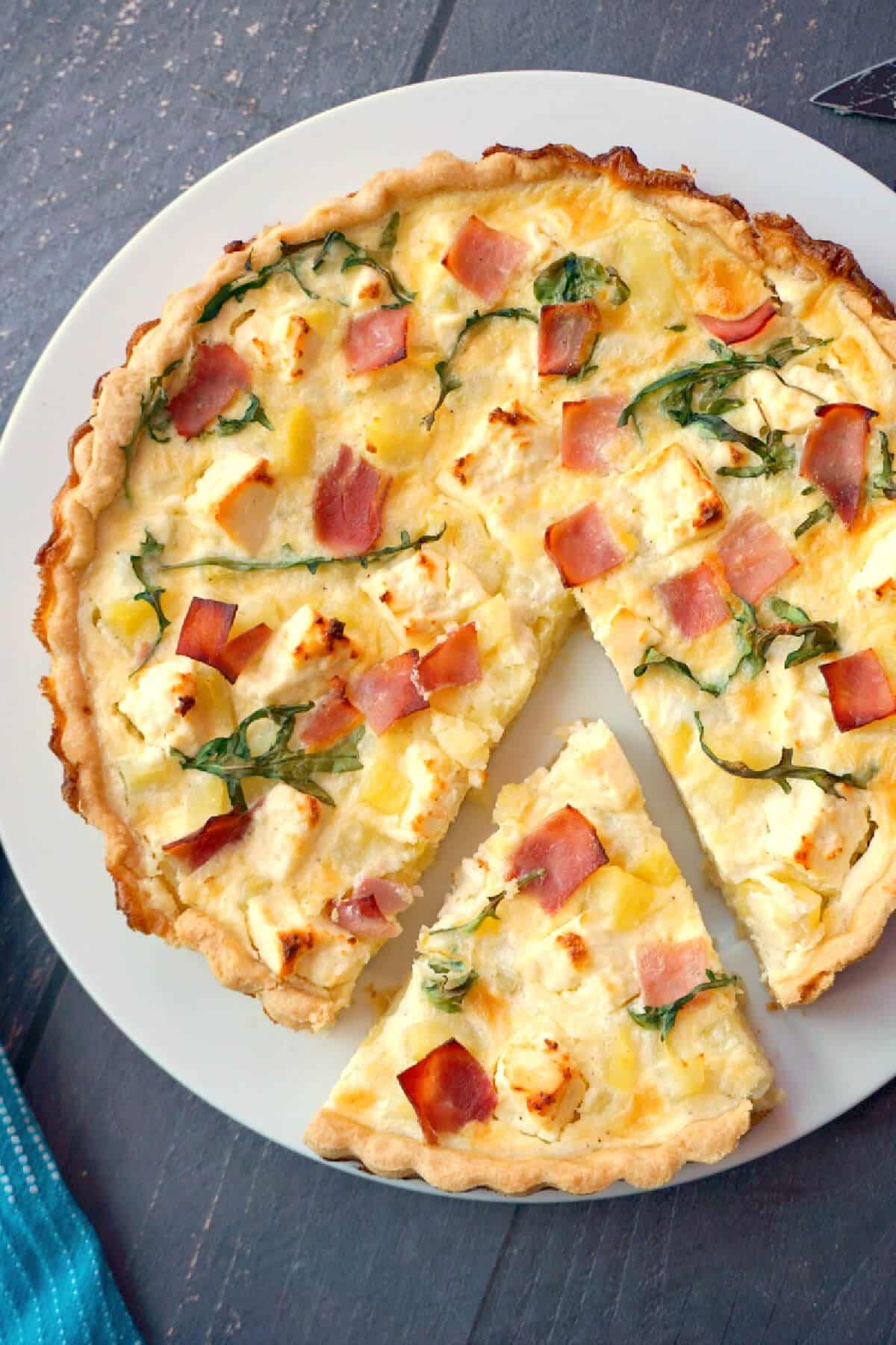 Overhead shoot of a white plate with a potato and ham quiche and a slice being cut off it.