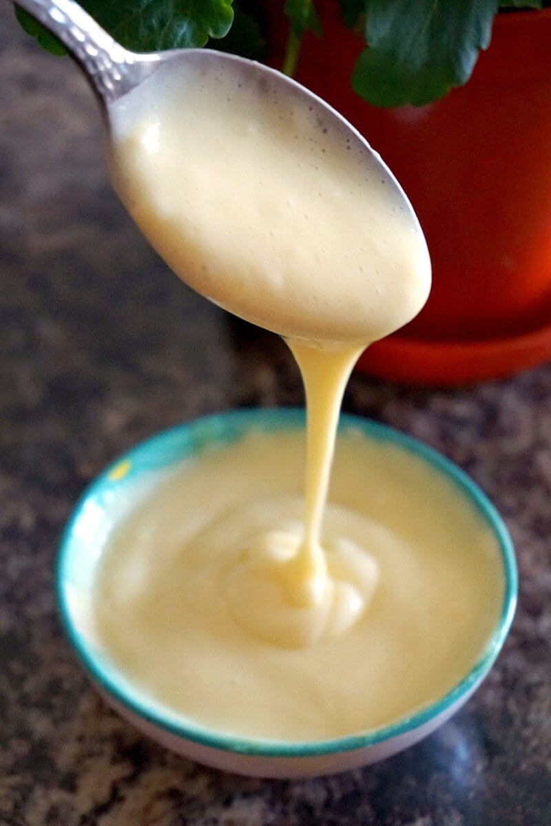 A small white bowl with custard being poured from a spoon.