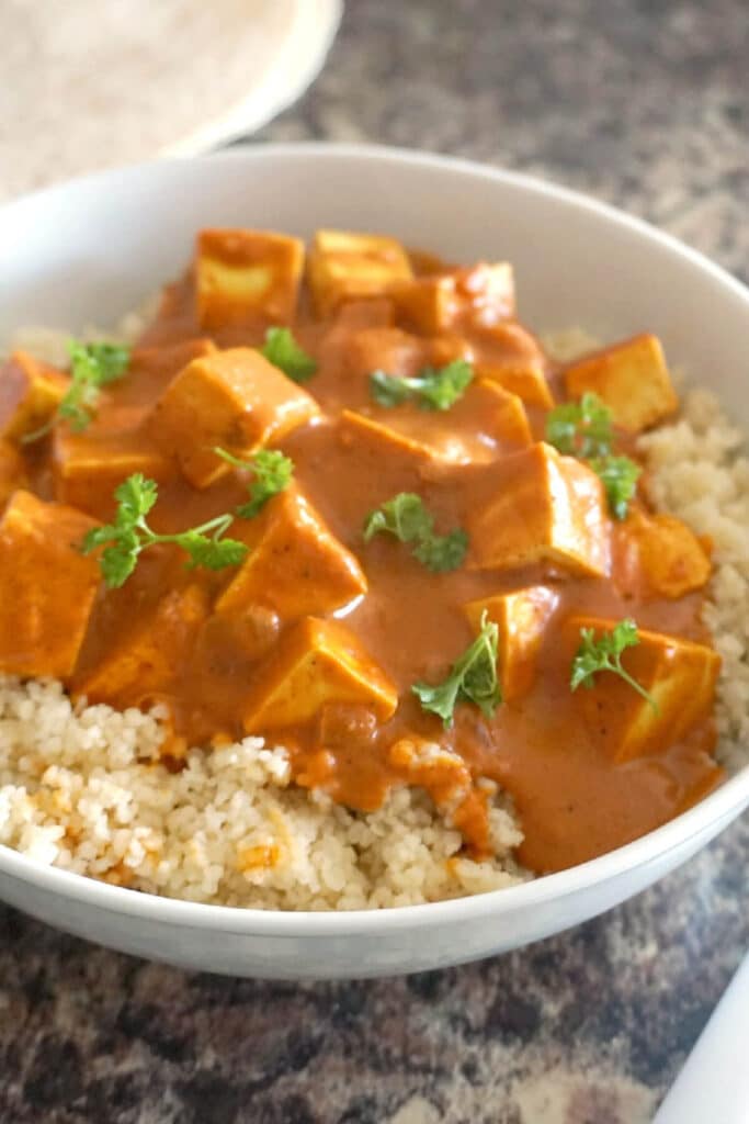 A white bowl with tofu curry over a bed of couscous