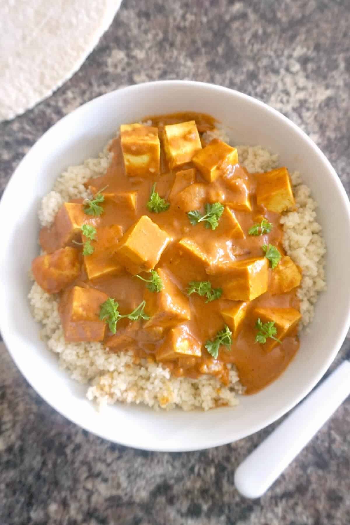 Overhead shoot of a white bowl with tofu curry over a bed of couscous.