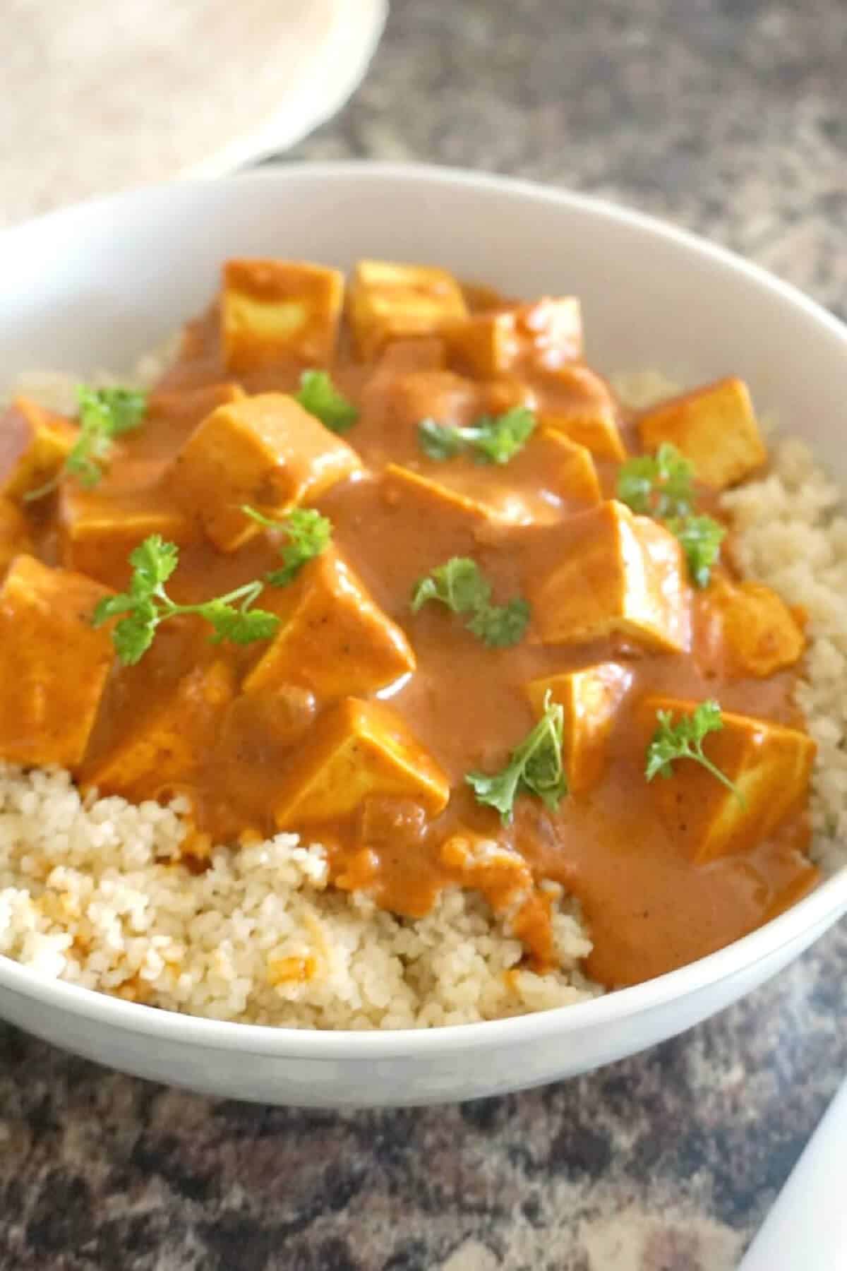 A white bowl with tofu curry over a bed of couscous.