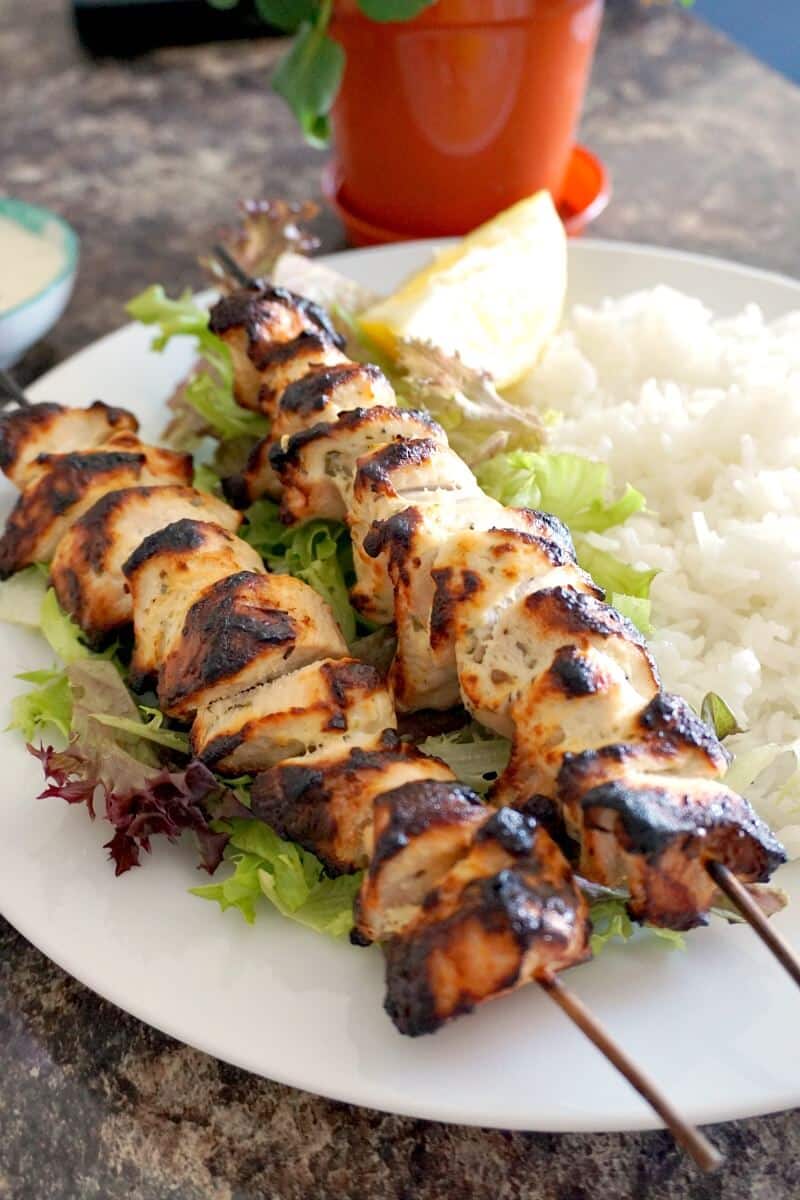 2 chicken kebabs on a bed of rice and salad.