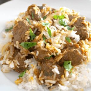 A white plate with beef and rice biryani