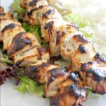 2 chicken kebabs on a bed of rice and salad