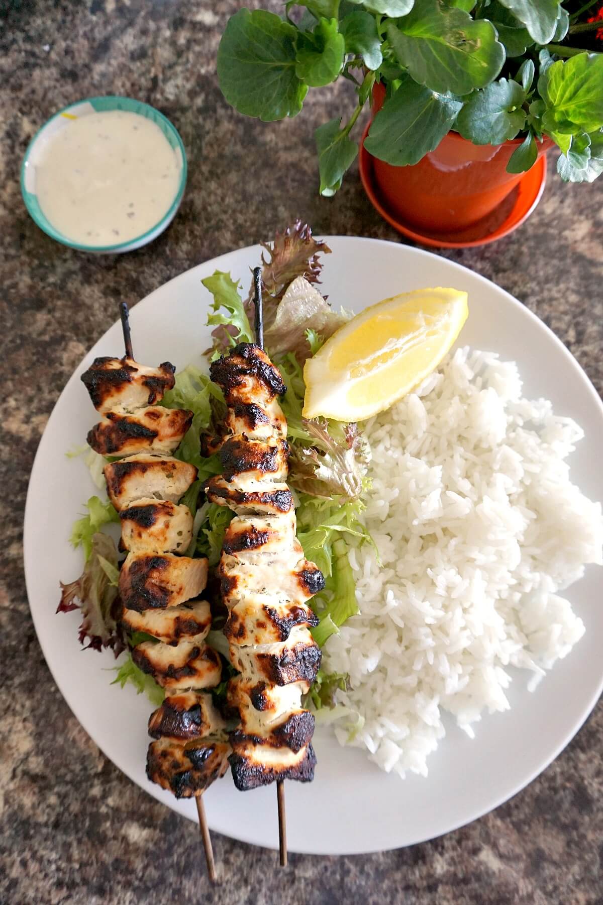 Overhead shoot of a white plate with 2 chicken kebabs, rice, salad and a lemon wedge