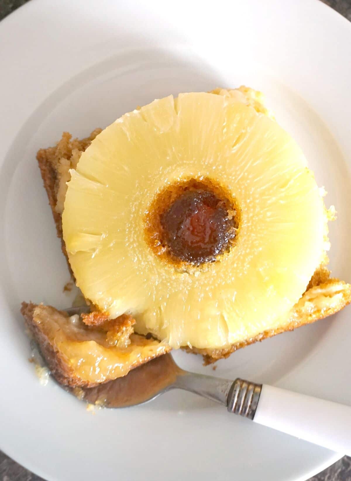 Overhead shoot of a white plate with a slice of pineapple upside down cake.