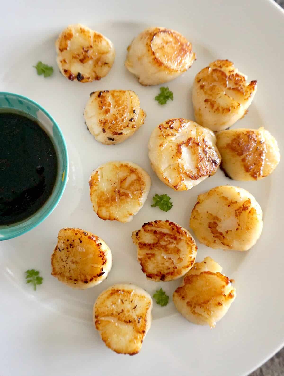 Overhead shoot of a white plate with seared scallops and a bowl with sauce.