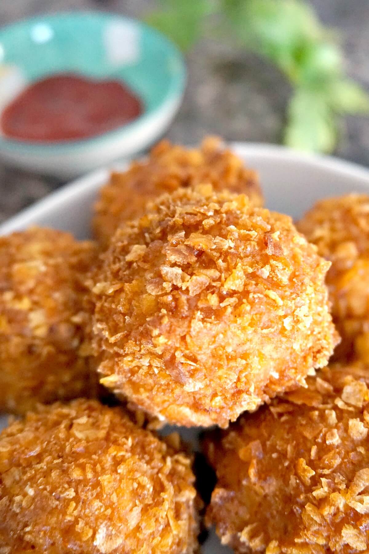 Popcorn chicken balls in a bowl with a small bowl with ketchup in the background.