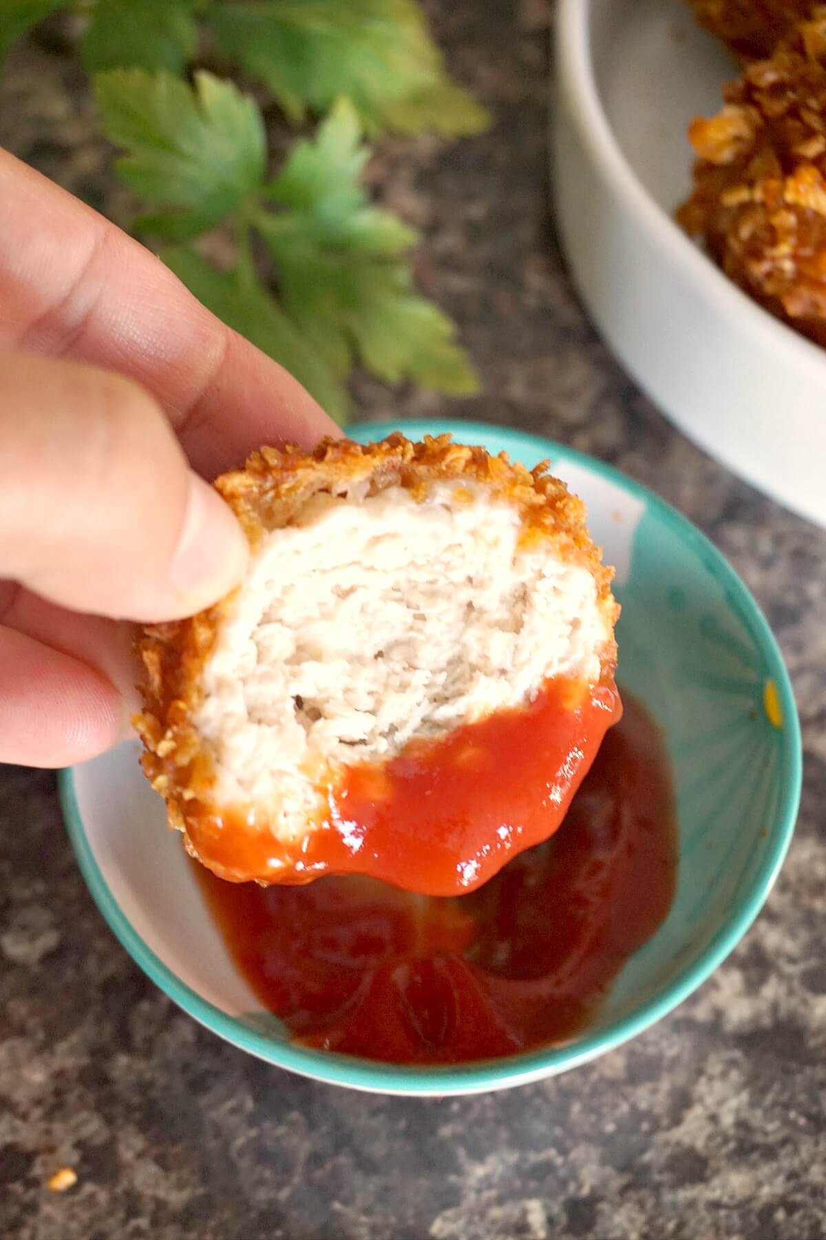 Half of a popcorn chicken bite in a small bowl with ketchup.