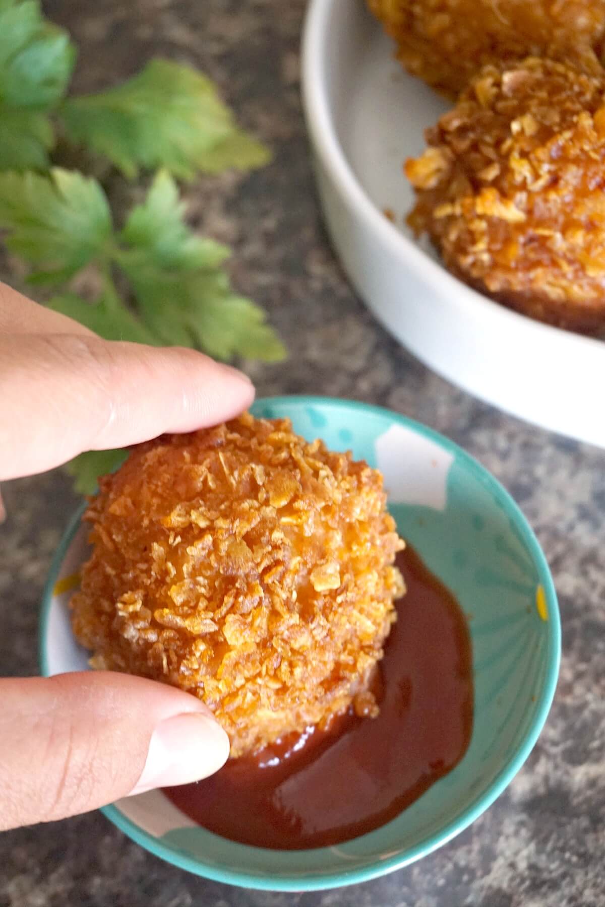 A popcorn chicken ball being dipped into ketchup.