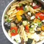 Overhead shoot of a white bowl with roasted vegetable pasta salad and feta