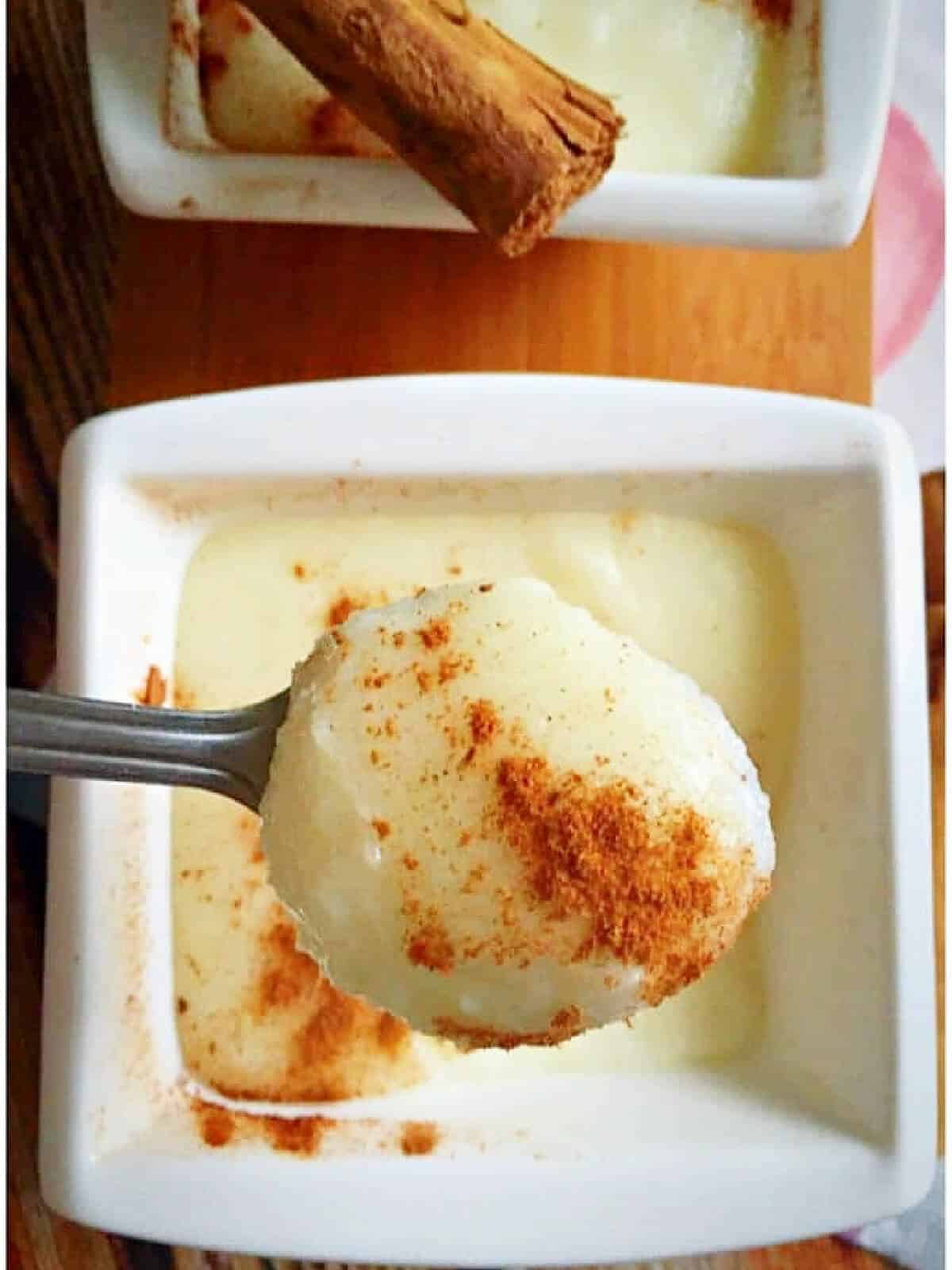 Overhead shoot of a white ramekin with semolina pudding and a teaspoon of pudding with ground cinnamon