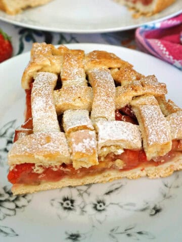 A white patterned plate with a slice of strawberry and rhubarb pie.