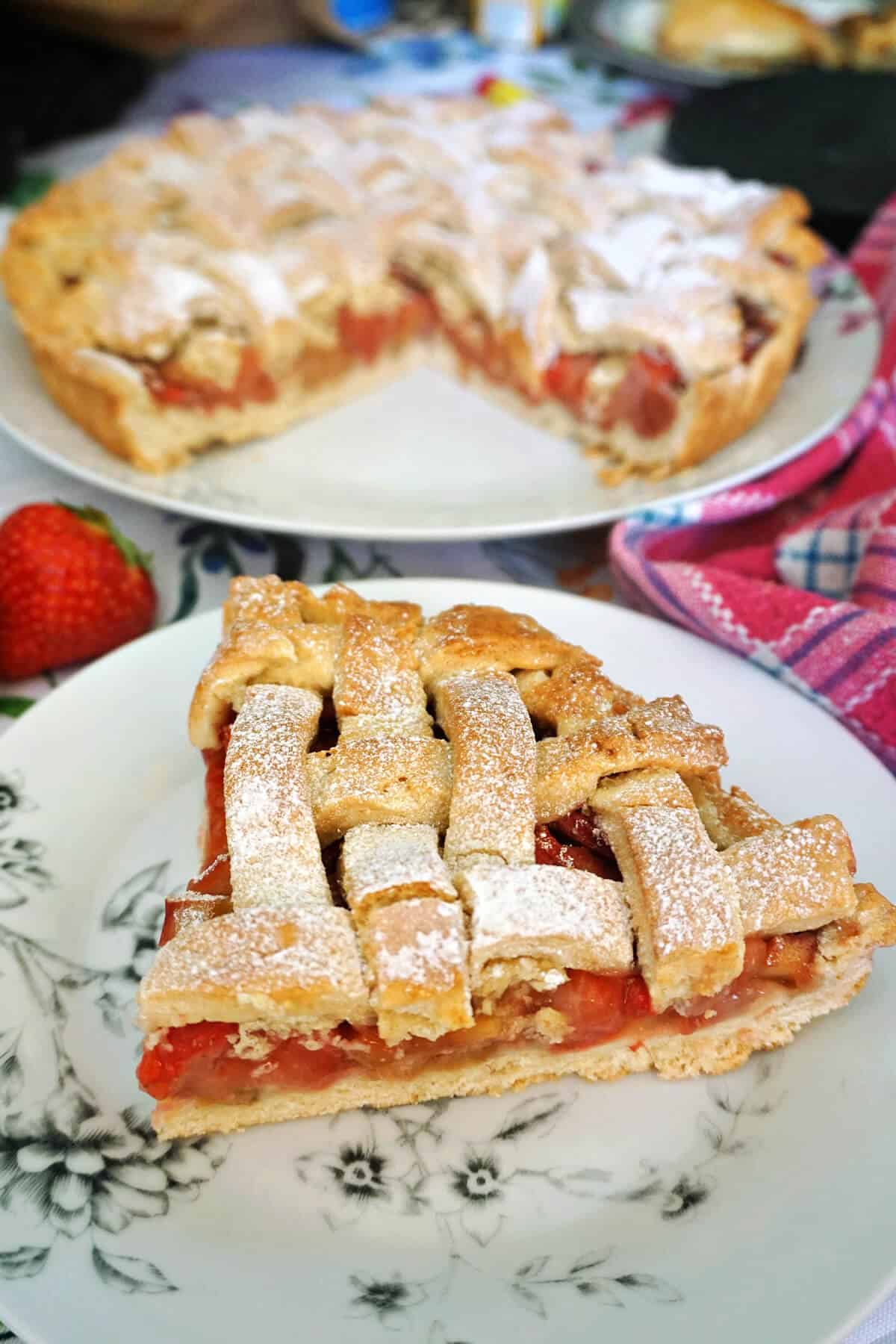 A white plate with a slice of fruit pie and a partially-visible larger plate with the rest of the pie.