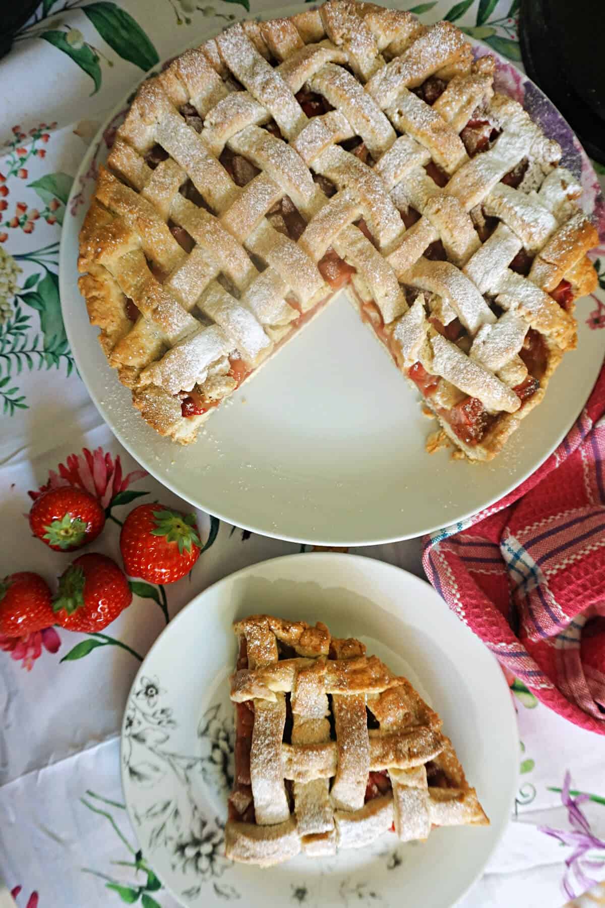 A small white plate with a slice of fruit pie, a larger plate with the rest of the pie and fresh strawberries around the plates.