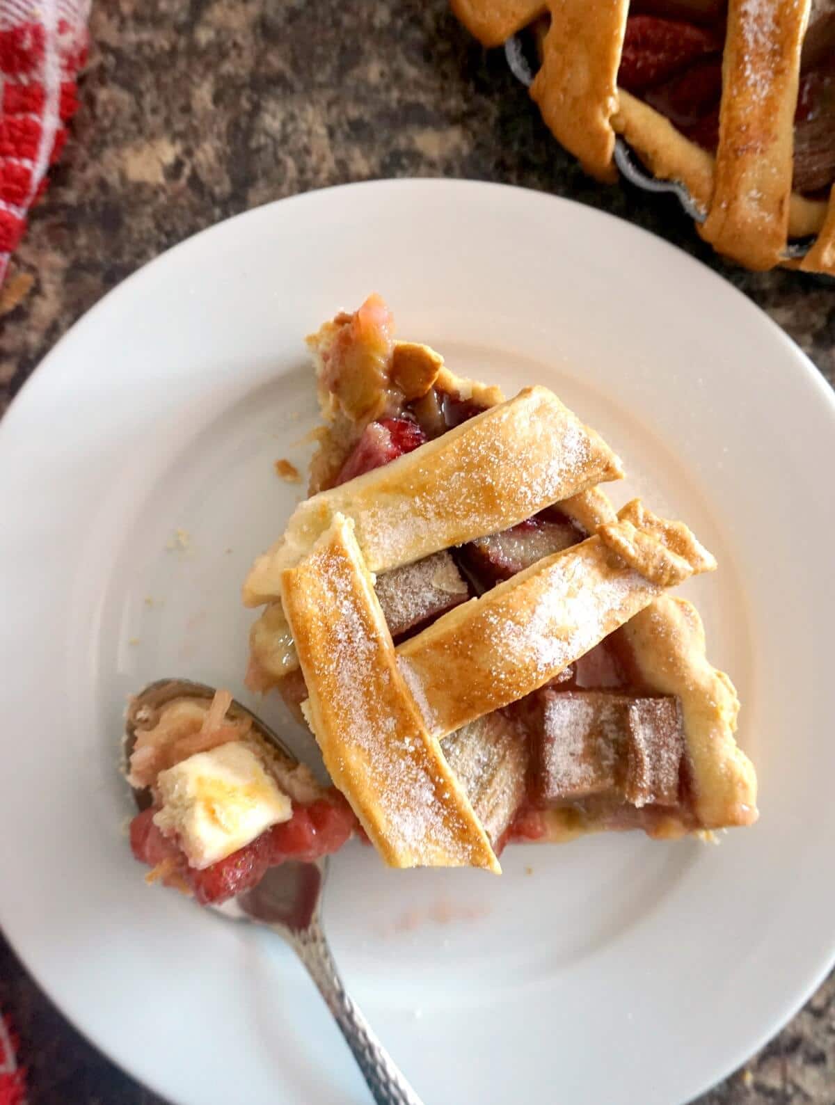 A white plate with a slice of strawberry rhubarb pie and a dessert spoon