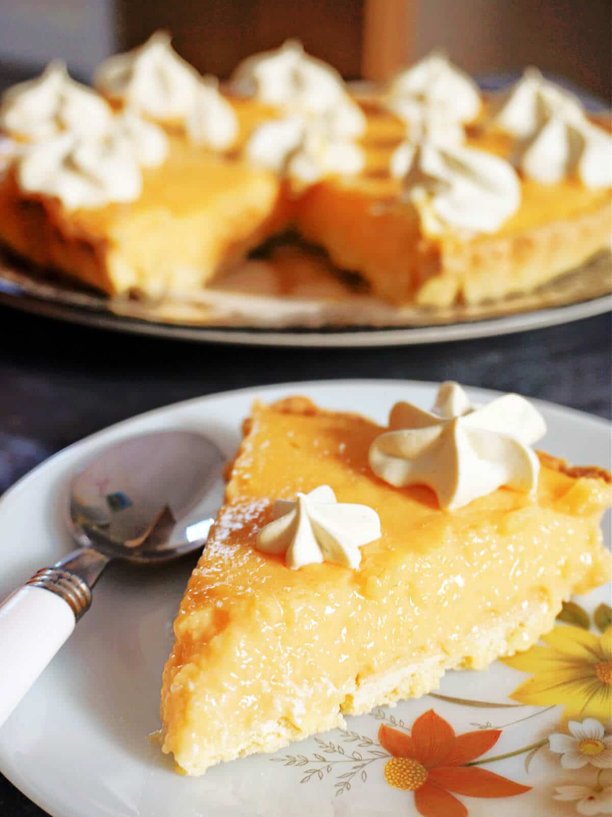 A slice of cantaloupe pie on a plate with a spoon on, and more pie in the background.