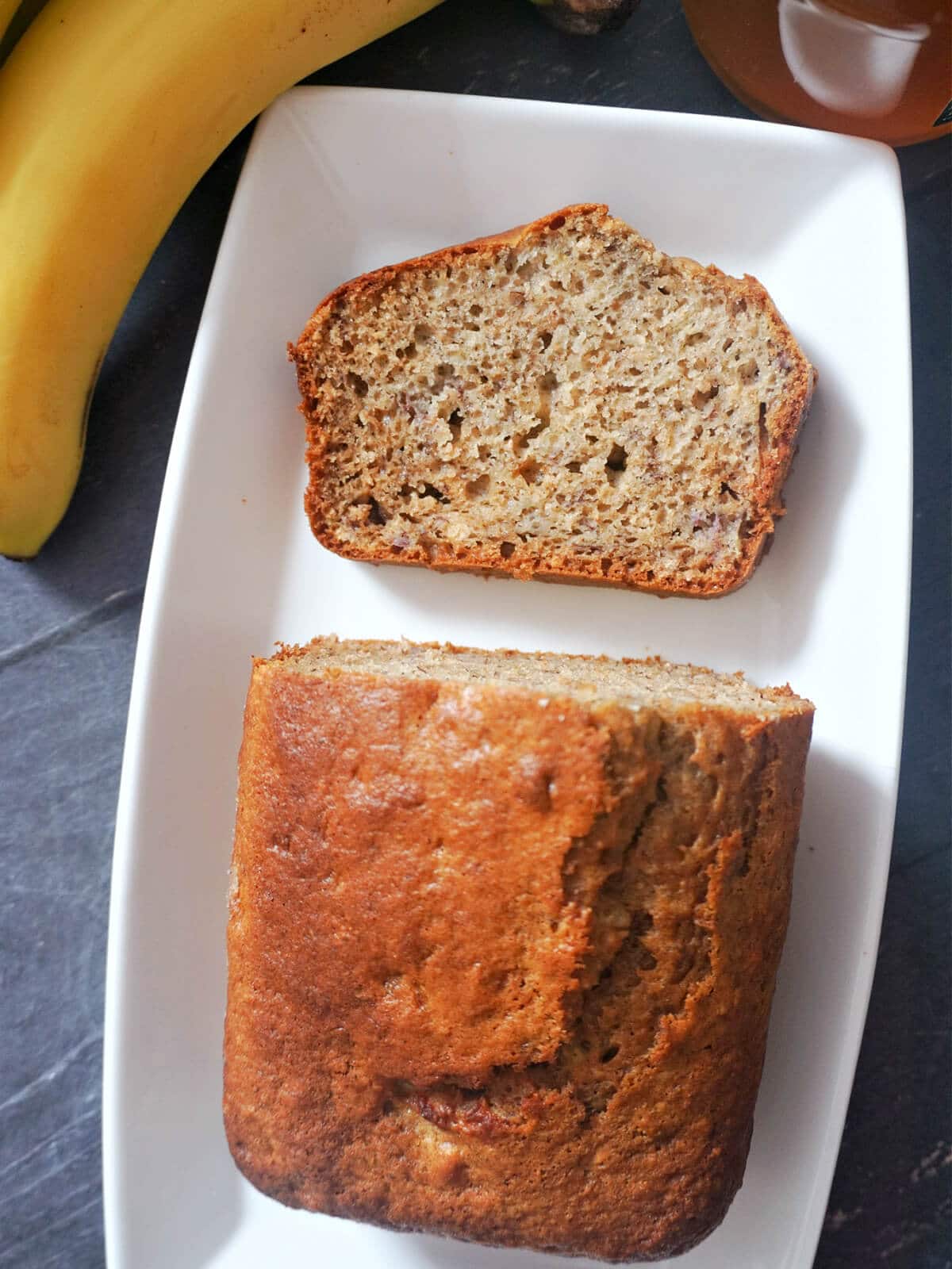 Overhead shot of a white rectangle plate with a slice of banana bread and the rest of the bread.
