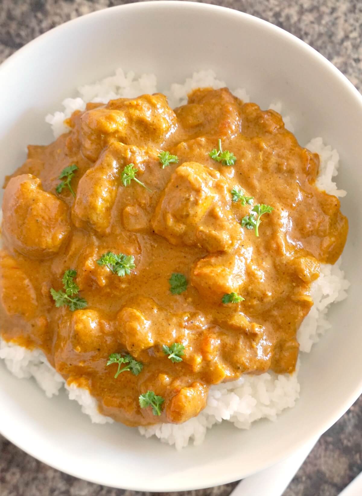 Overhead shoot of a white plate with fish curry over a bed of rice.