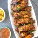 Overhead shoot of a white rectangle plate with chicken wings, a small white bowl of sauce next to it and one of yellow rice