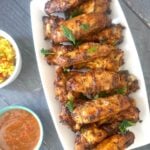 Overhead shoot of a white rectangle plate with chicken wings, a small white bowl of sauce next to it and one of yellow rice