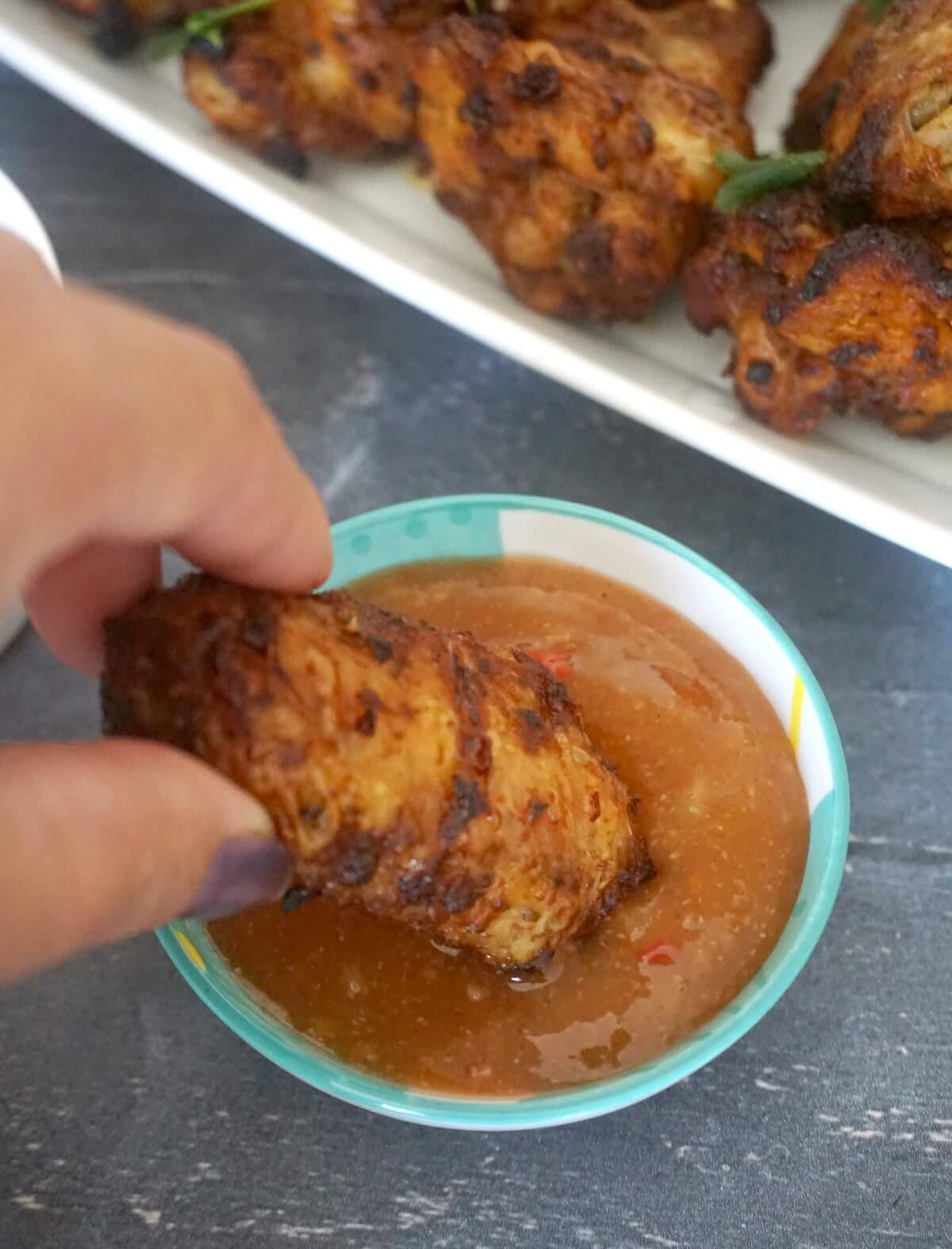 A chicken wing being dipped into a small bowl with sauce.