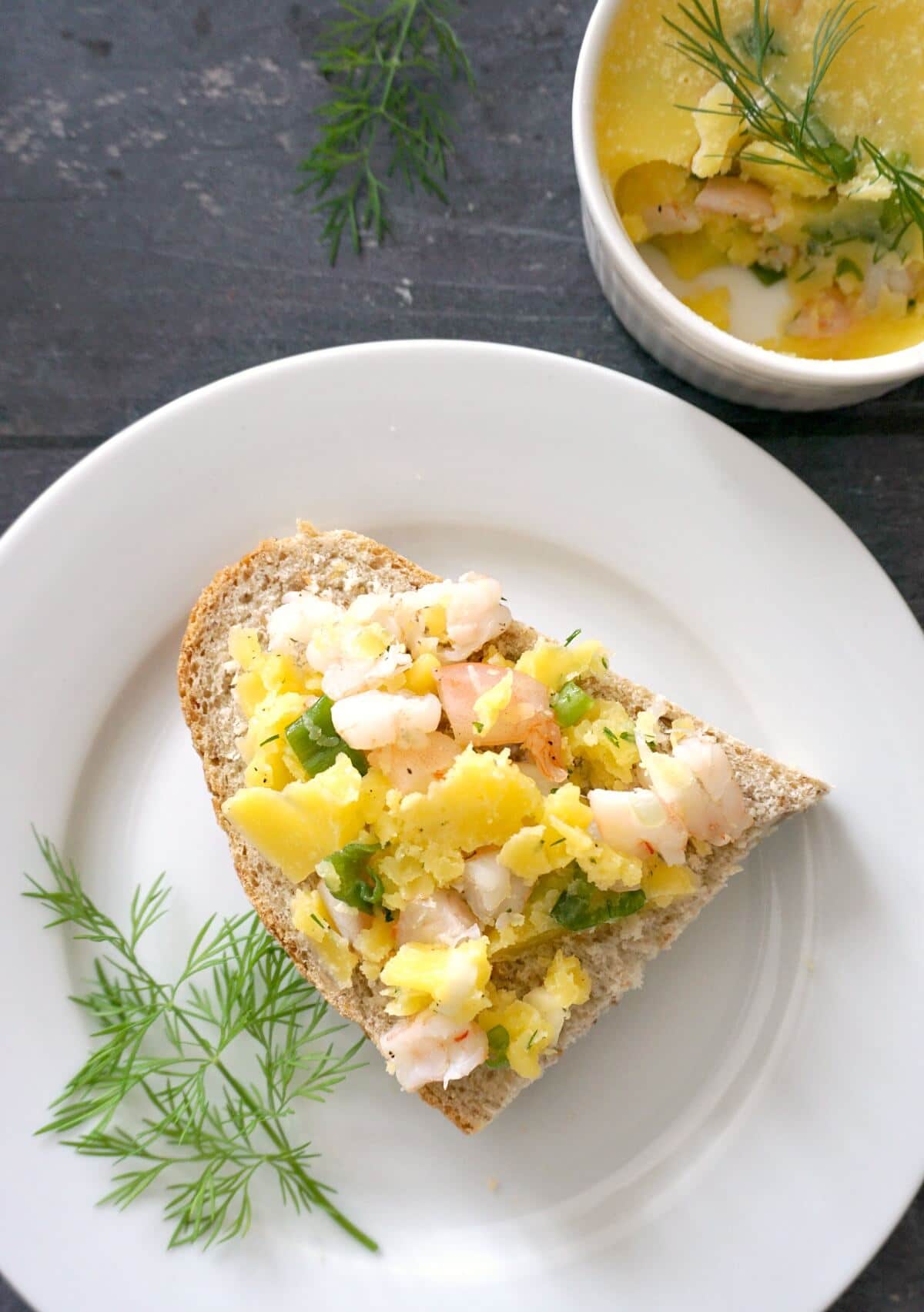 A slice of bread with potted shrimp spread over it, all arranged on a white plate with a dill sprig on it