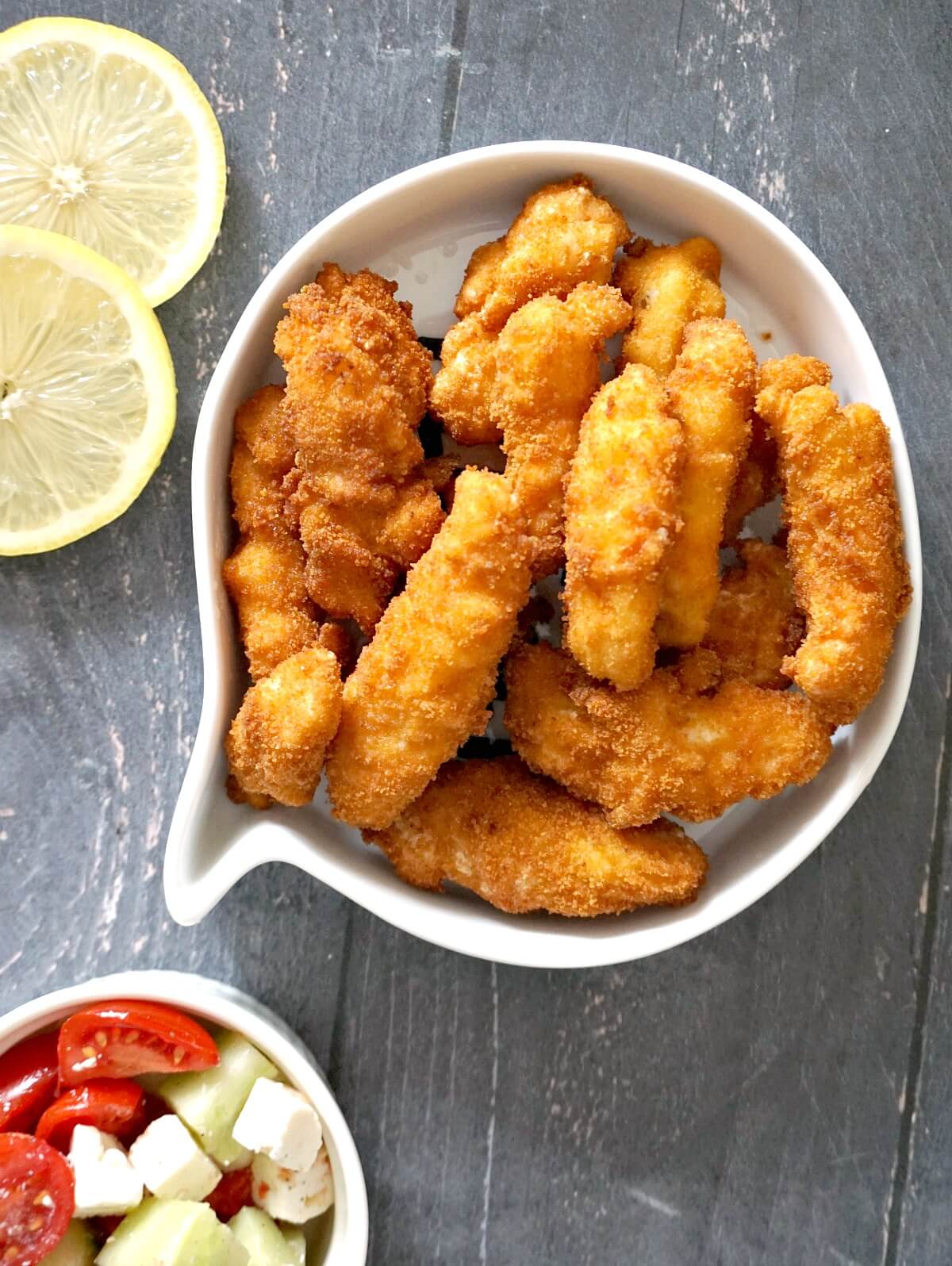 Overhead shoot of a white bowl with scampi, 2 lemon slices and a white small with tomato salad on the side.