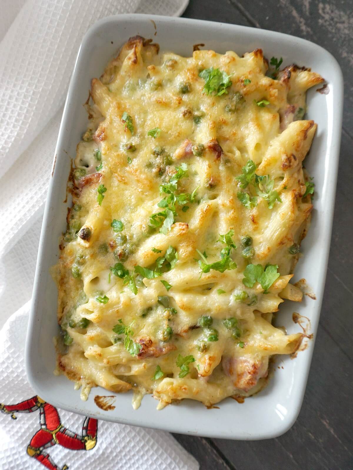 Overhead shoot of a dish with cheesy pasta bake with ham and peas.