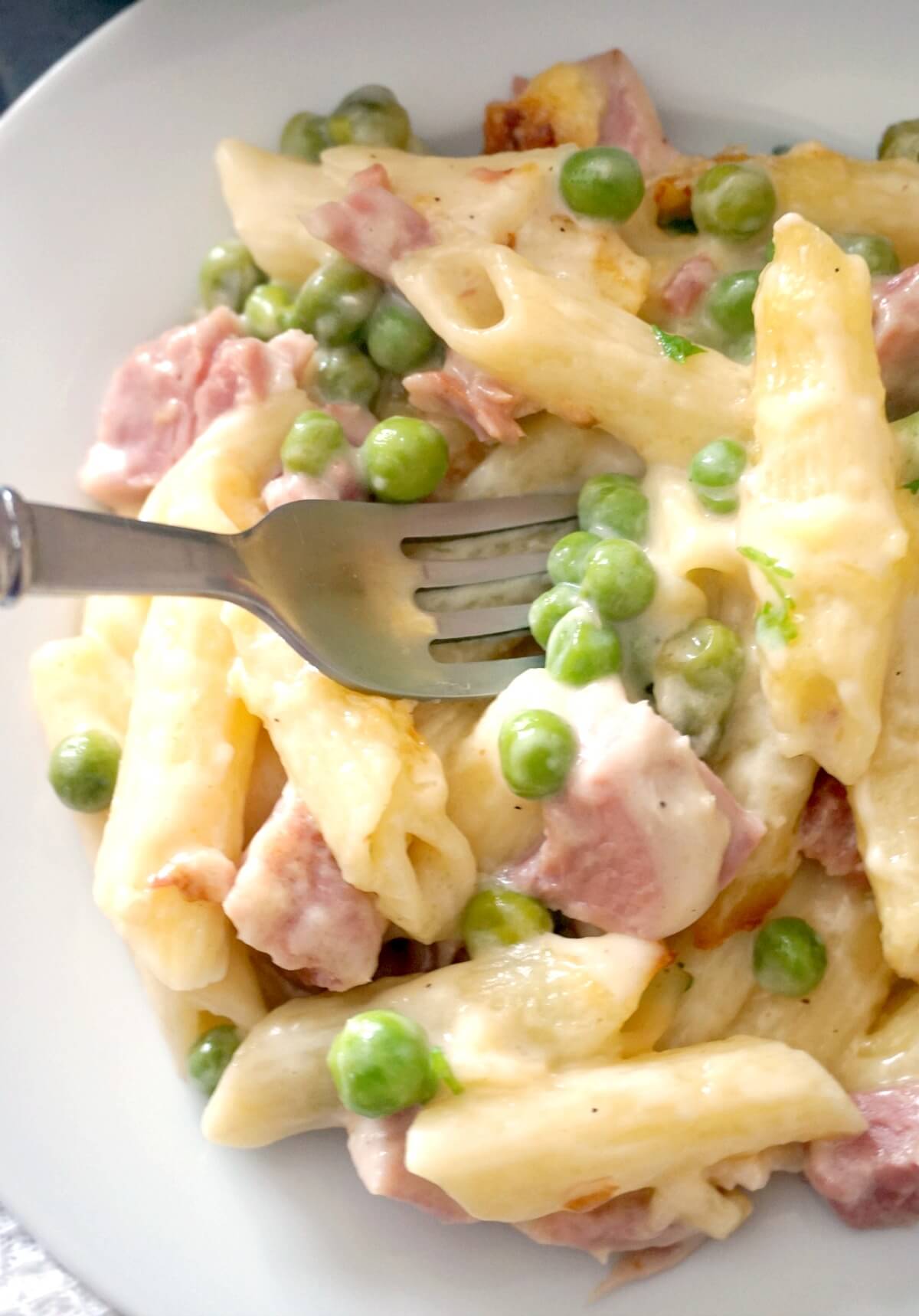 Cheesy ham and pea pasta on a white plate.