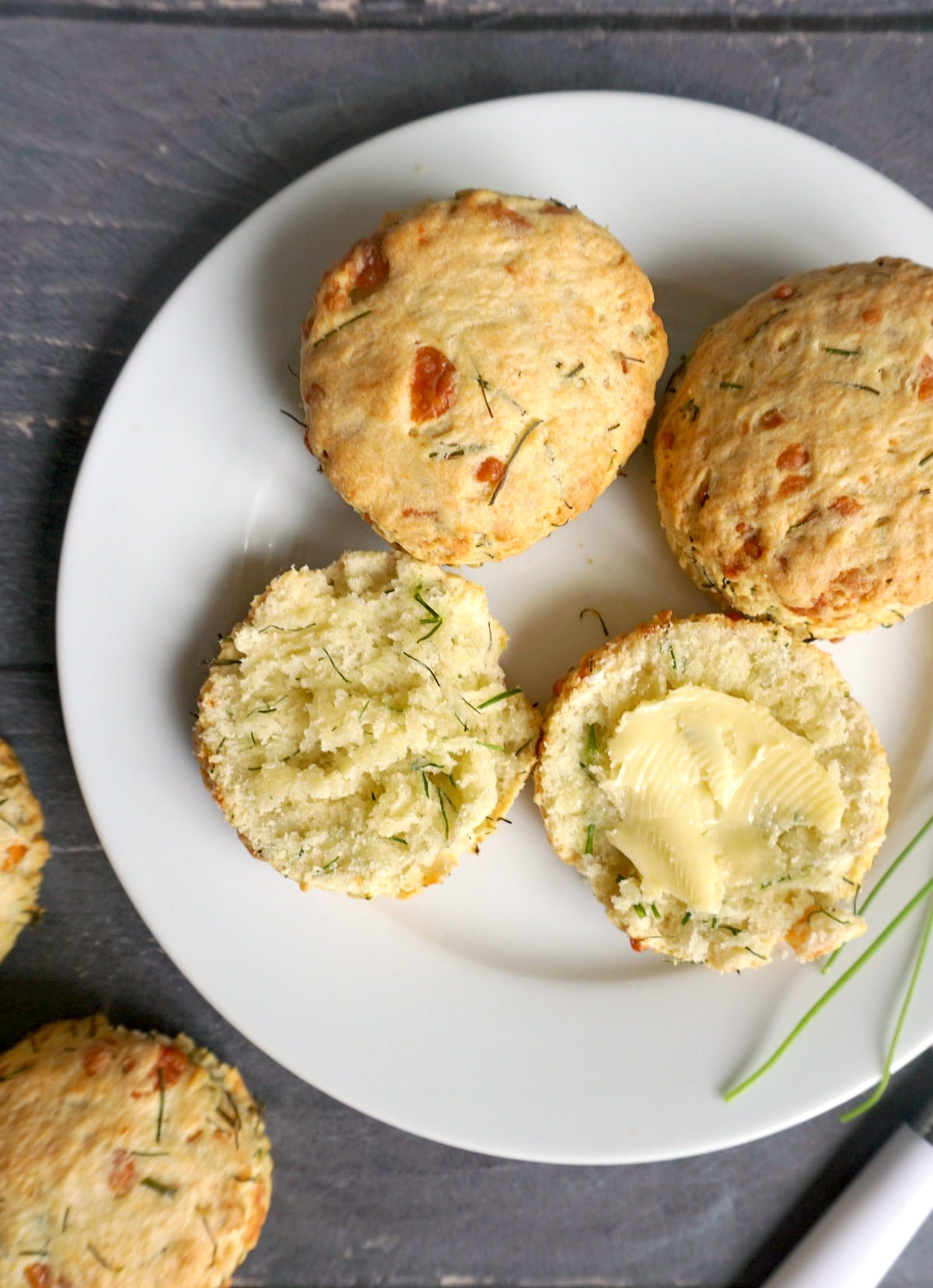 Overhead shoot of a white plate with 2 halves of scones spread with butter, and 2 whole scones.