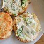A white plate with 2 halves of a scone topped with herb butter and a whole scone partially visible.