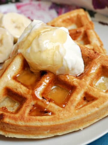 2 waffles on a white plate topped with a dollop of yogurt and honey