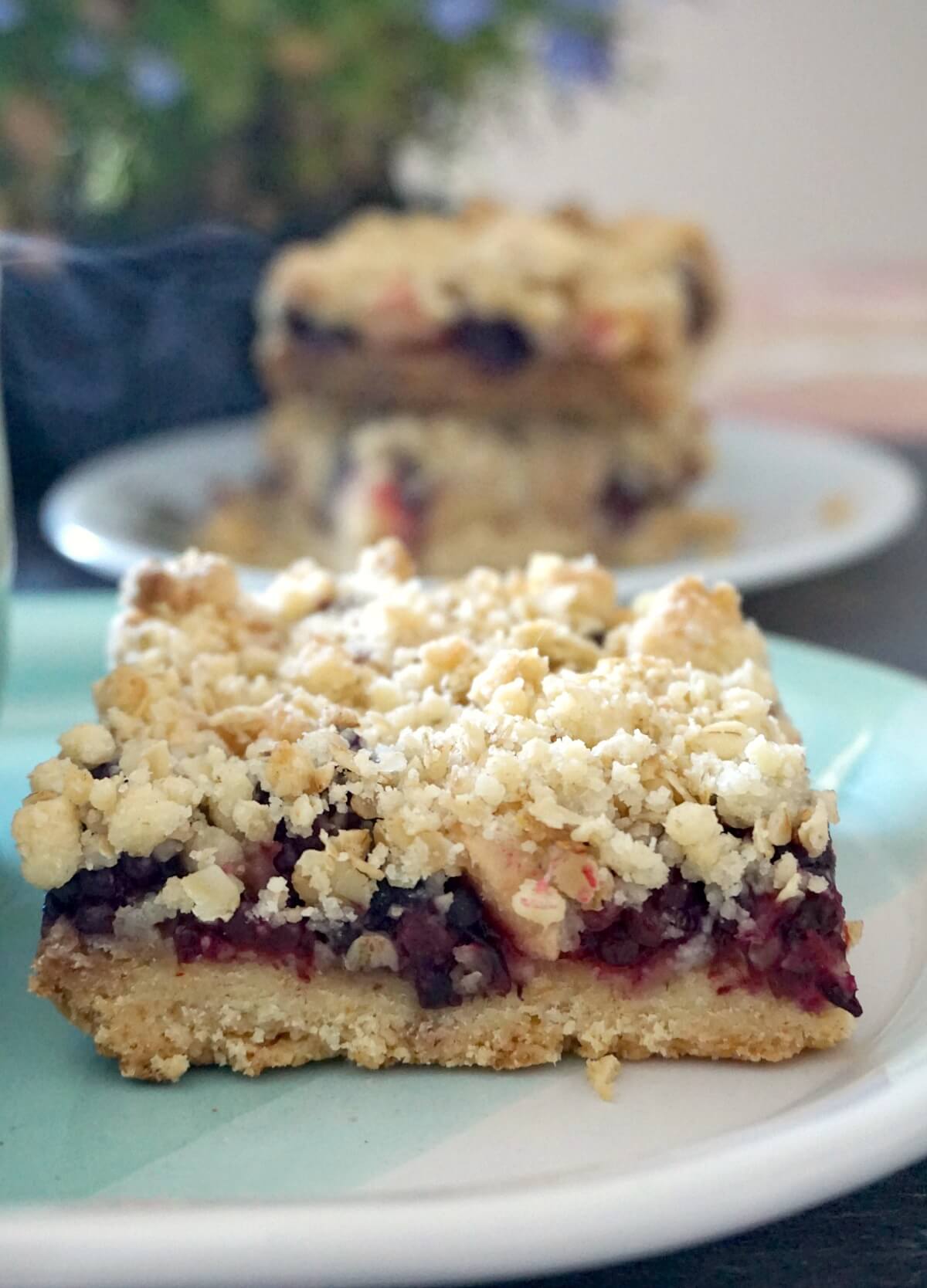 A slice of apple and blackberry crumble bar on a light blue plate.
