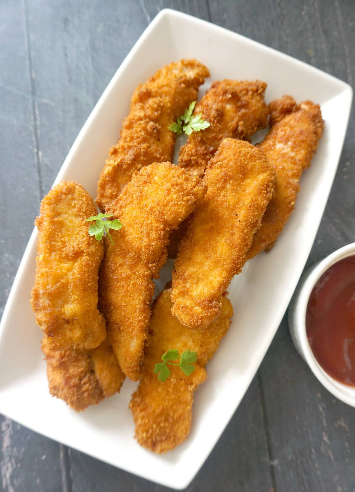 Overhead shoot of a white rectangle plate with chicken tenders.