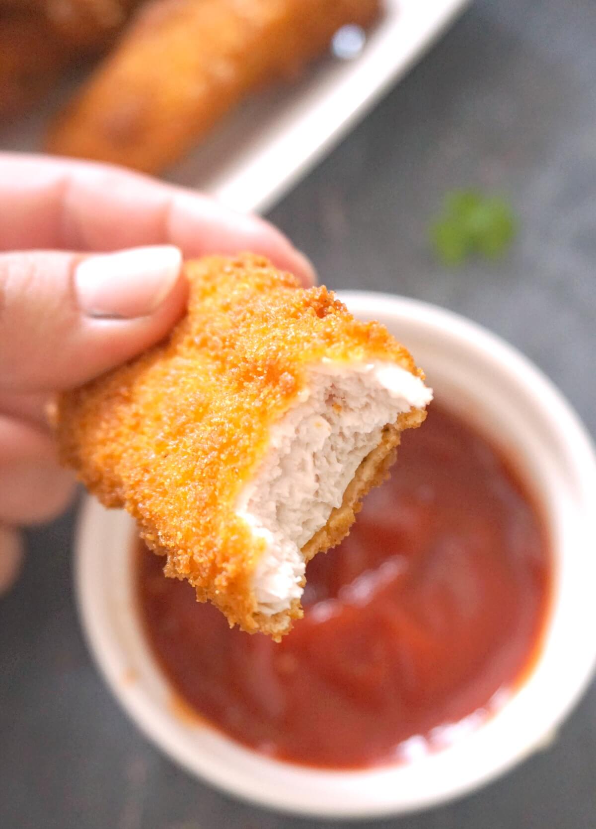 Half of a chicken tender over a bowl of ketchup