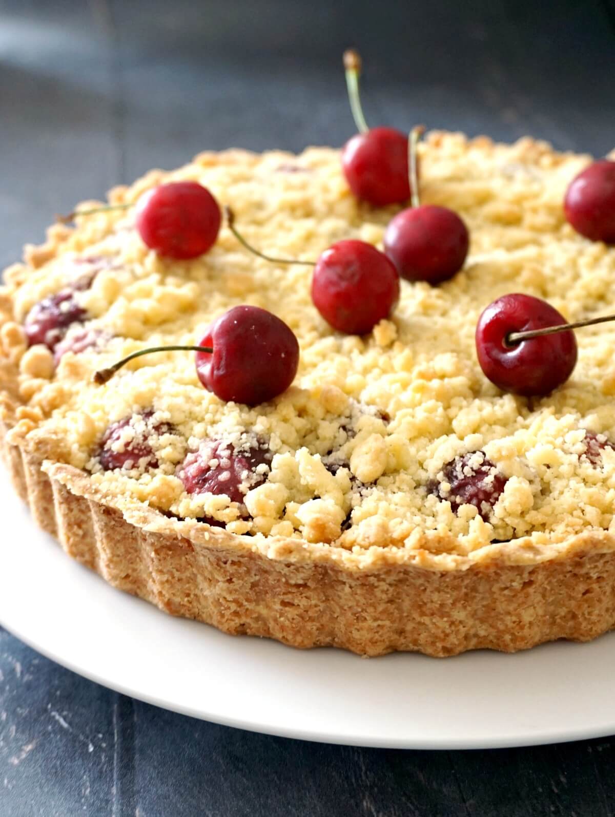 A pie on a white plate with cherries on top.