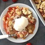 Overhead shoot of a white plate with crumble topped with vanilla ice cream and a spoon in it