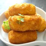 A white plate with 5 potato croquettes and 2 parsley leaves on top