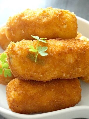 A white plate with 5 potato croquettes and 2 parsley leaves on top