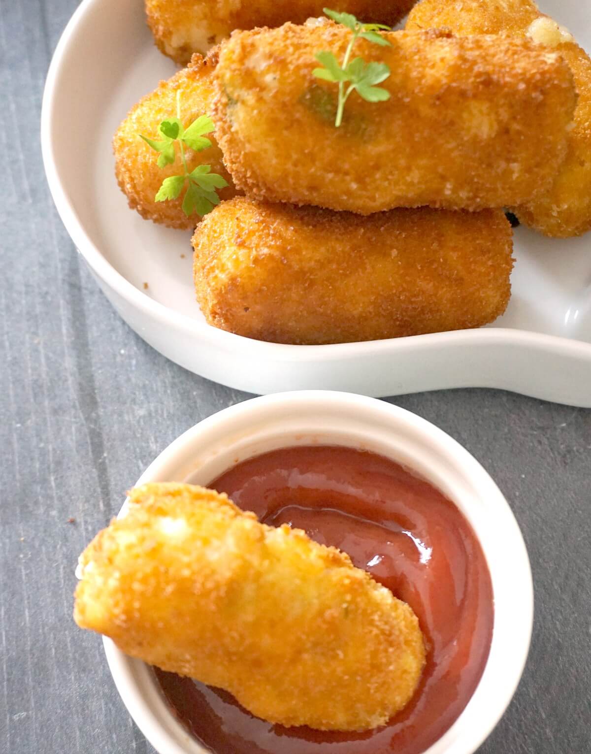 A small bowl with ketchup and a croquette, and another bowl with more croquettes.