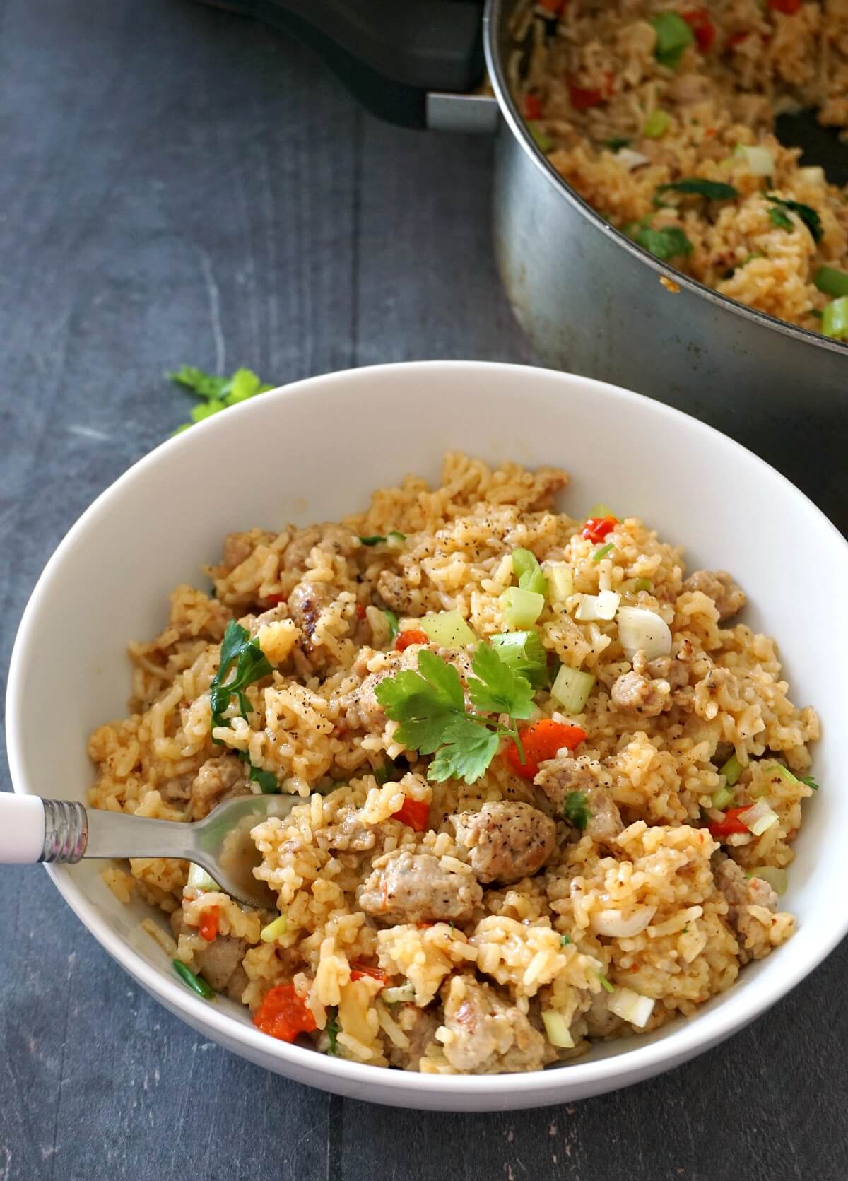 A white bowl with rice and a pot with more rice in  he background.