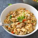 A white pot with sausage rice garnished with a parsley leaf