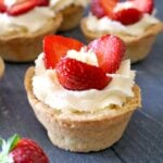 A mini tart with cream, custard and 3 strawberry slices with other tarts in the background